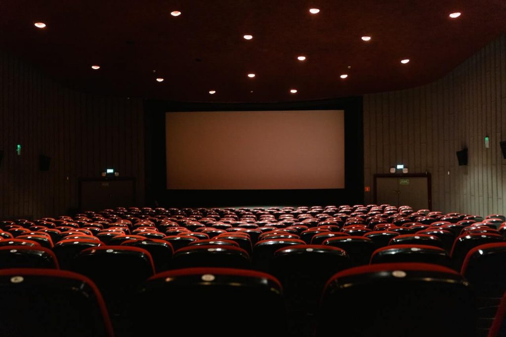 An image of an empty movie theater with bright lights illuminating the iconic red chairs.
